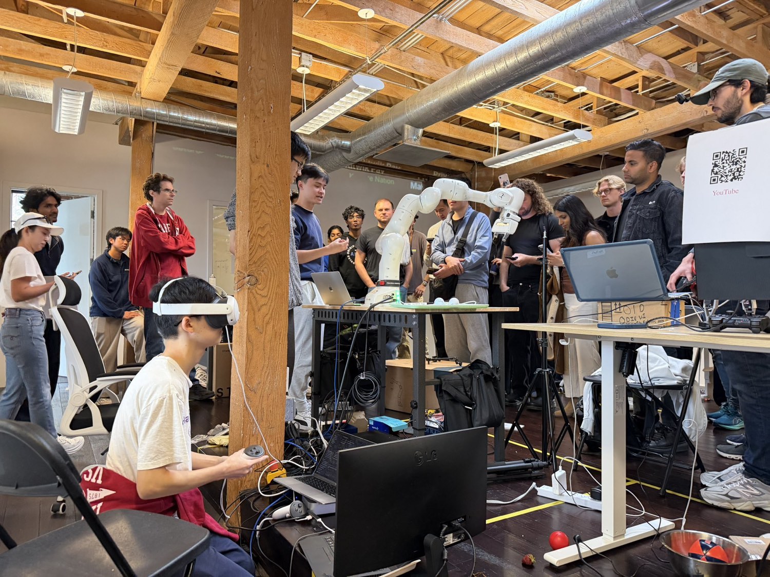 A crowd around a Franka arm on demo day, one builder driving it in a VR headset